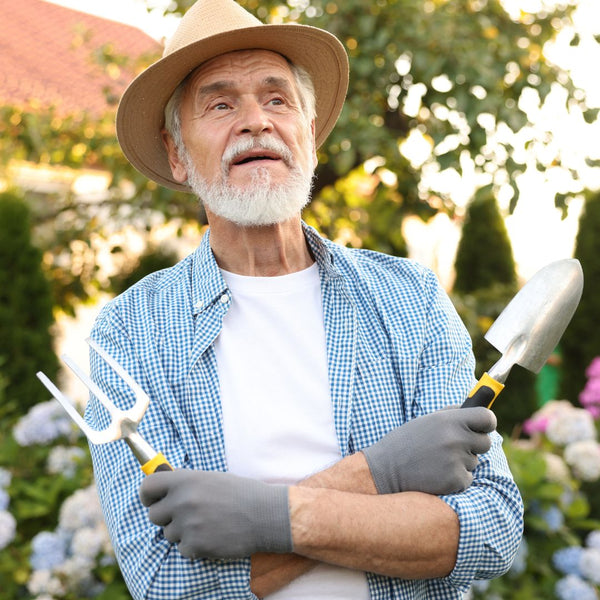 Man in a garden holding gardening tools with a blurred background of plants and flowers